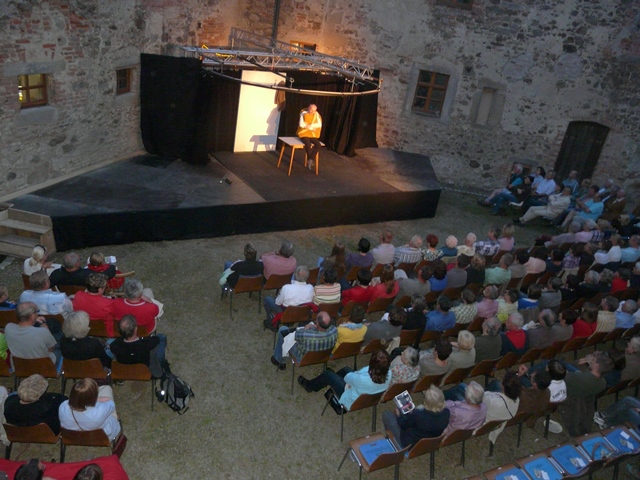 Foto von einer Aufführung mit Schauspielern auf der Bühne und Menschen im Publikum