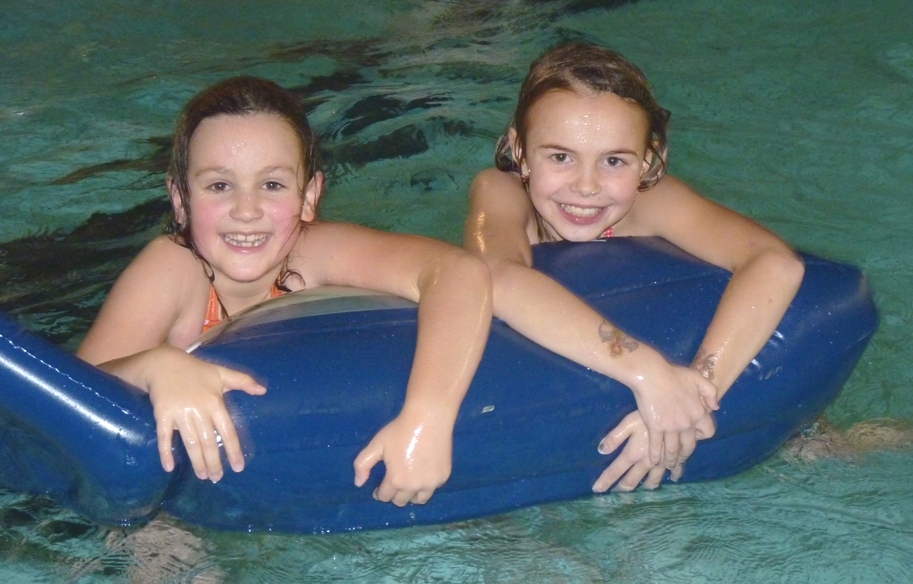 Zwei Kinder im Wasser halten sich an einer Schwimmhilfe fest und blicken in die Kamera