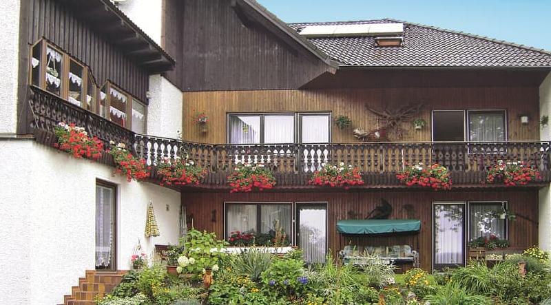 Beispiel-Foto eines Gastgeberhaus aus Moosbach mit großem Holzbalkon, holzvertäfelter Fassadenverkleidung und einem üppig grünem Garten