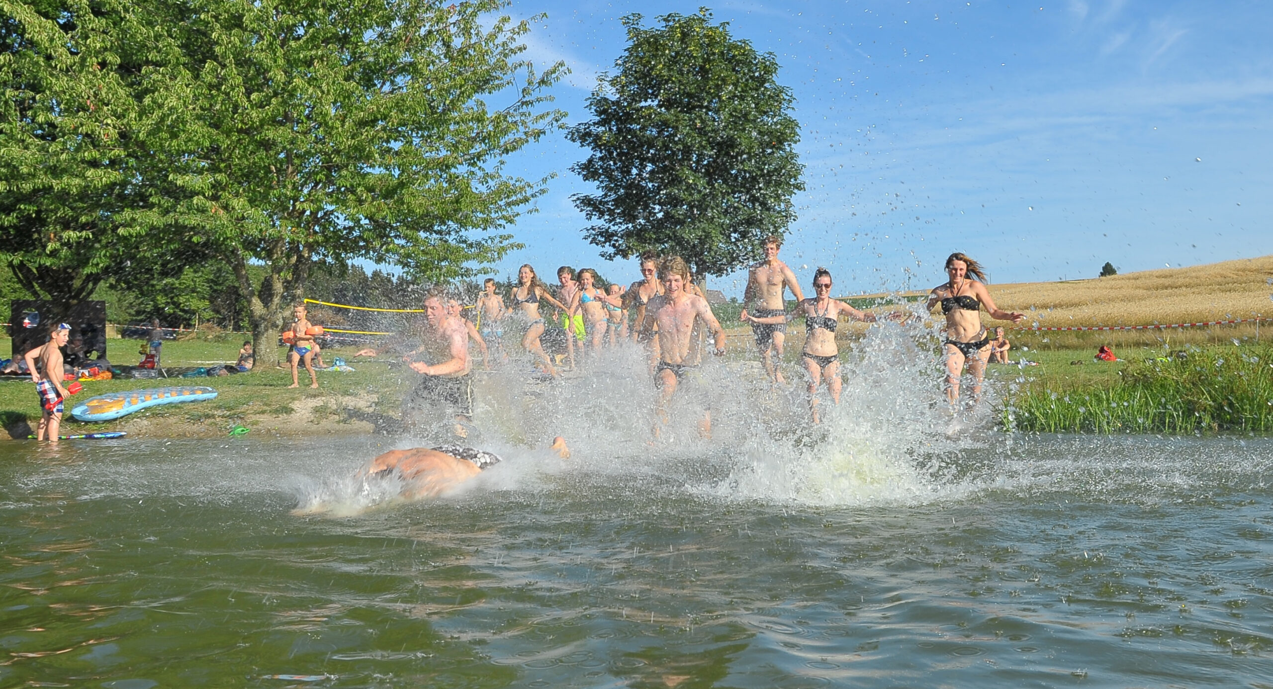 Jugendliche laufen in die Naturbadestelle Tröbes. Das Wasser spritzt.